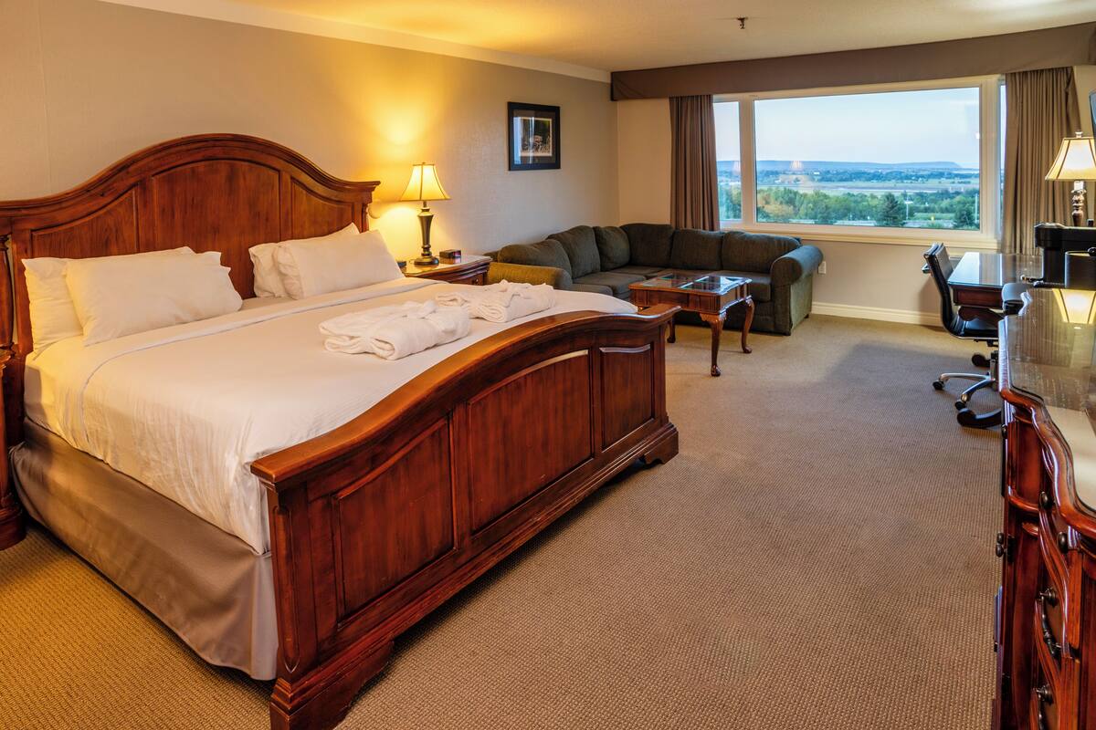 Habitación de hotel con una cama grande, un sofá, un escritorio y vistas al exterior.