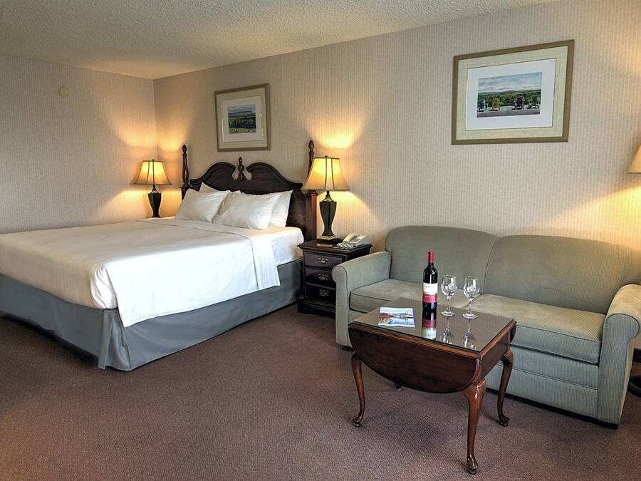 Une chambre d’hôtel avec un lit, un canapé, une table basse avec une bouteille et des verres, et deux lampes.