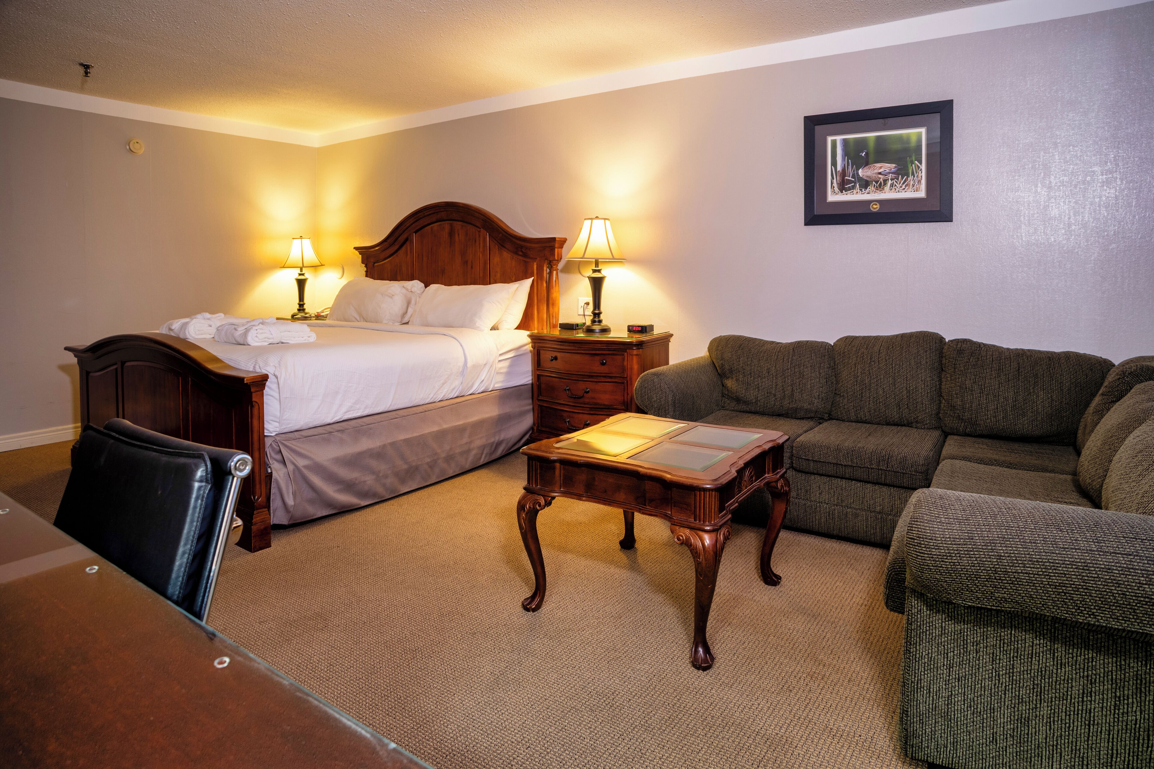 Una habitación de hotel con cama, mesitas de noche con lámparas, un sofá y una pequeña mesa.
