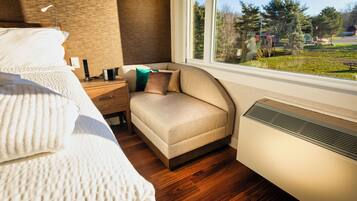 A bedroom with a bed, bedside table, lamp, and a view of a park through a window.