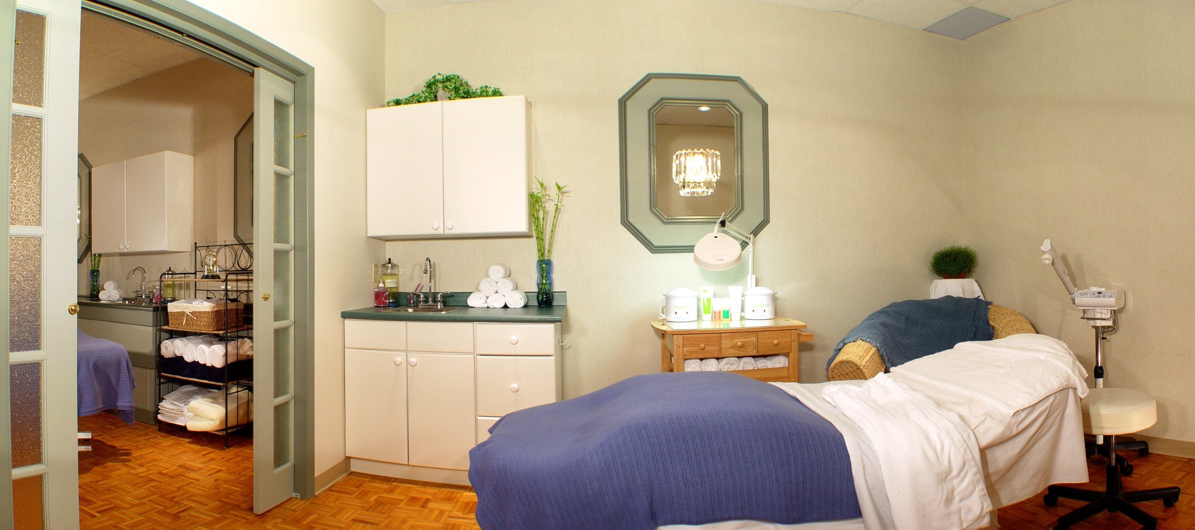A hotel room with a bed, a desk, a chair, a mirror, and a small cabinet.