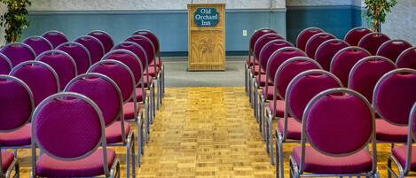 A conference room with rows of purple chairs and a wooden podium labeled "Old Orchard Inn".