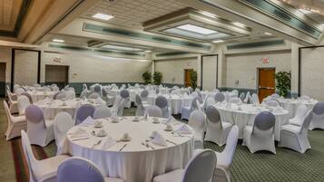 A banquet hall with round tables set for dining, white chairs, and exit signs on the walls.
