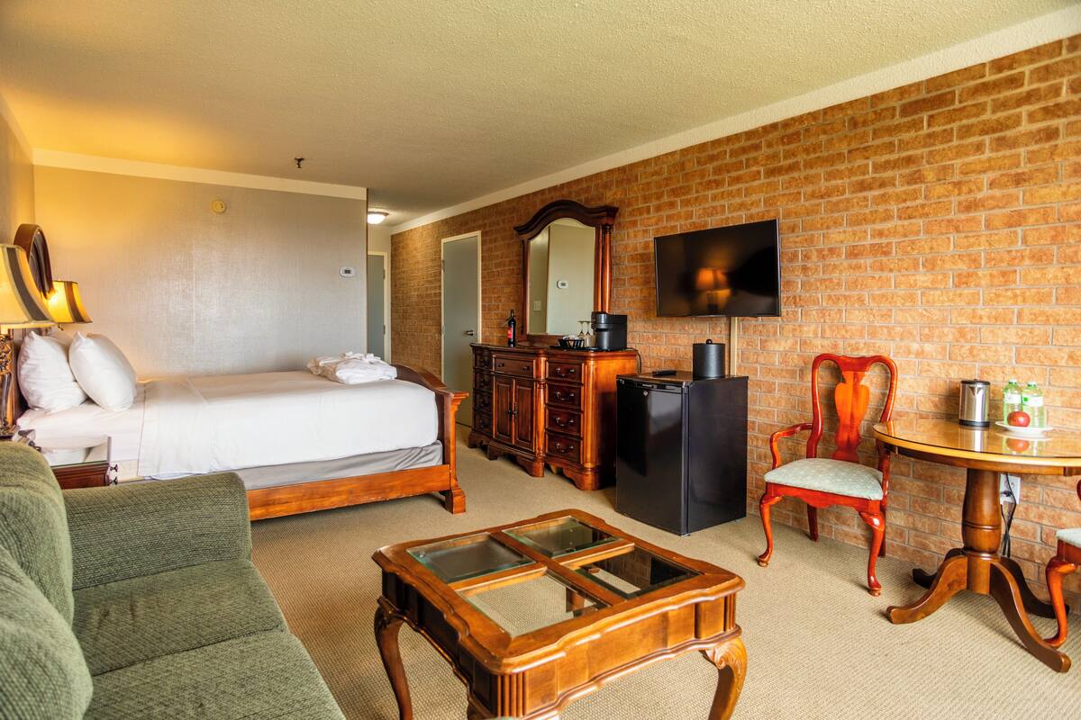Habitación de hotel con una cama, un aparador de madera, un televisor, una mesa de comedor y un sofá verde.
