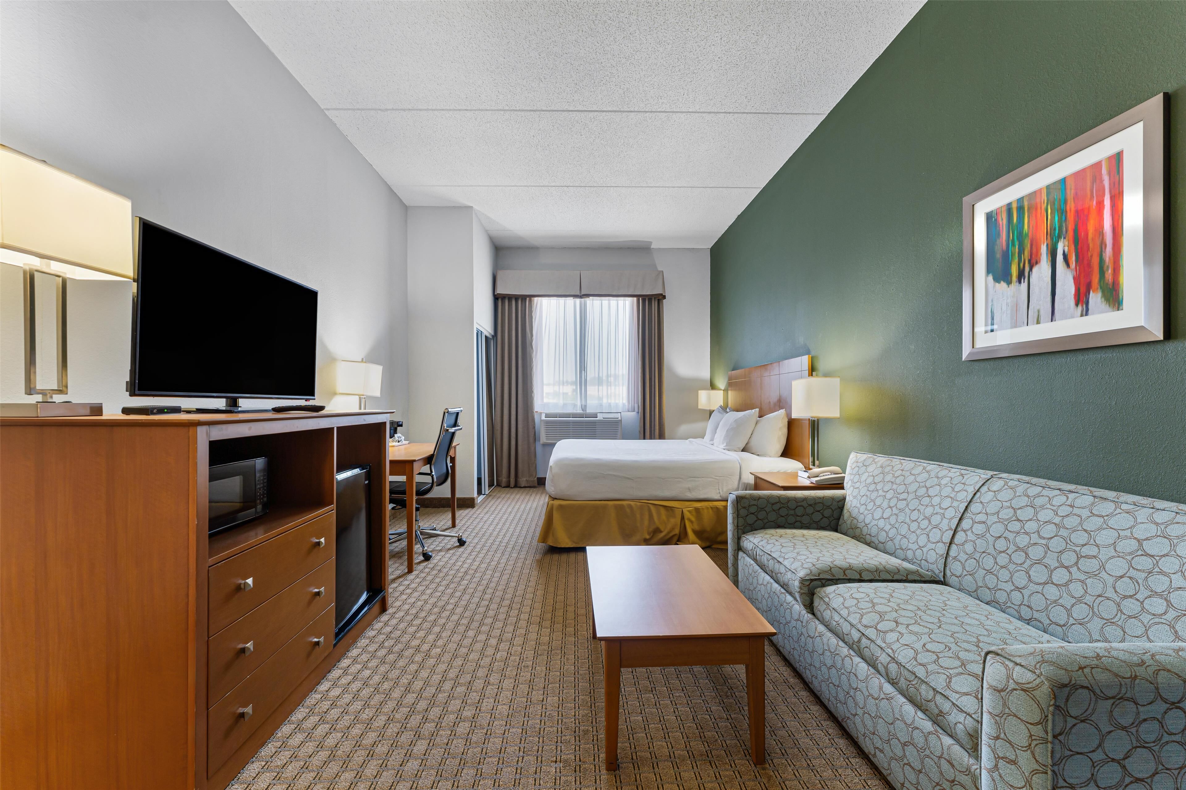 Habitación de hotel con cama, sofá, escritorio, televisor y un cuadro en la pared.