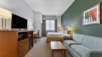 Habitación de hotel con cama, sofá, escritorio, televisor y un cuadro en la pared.