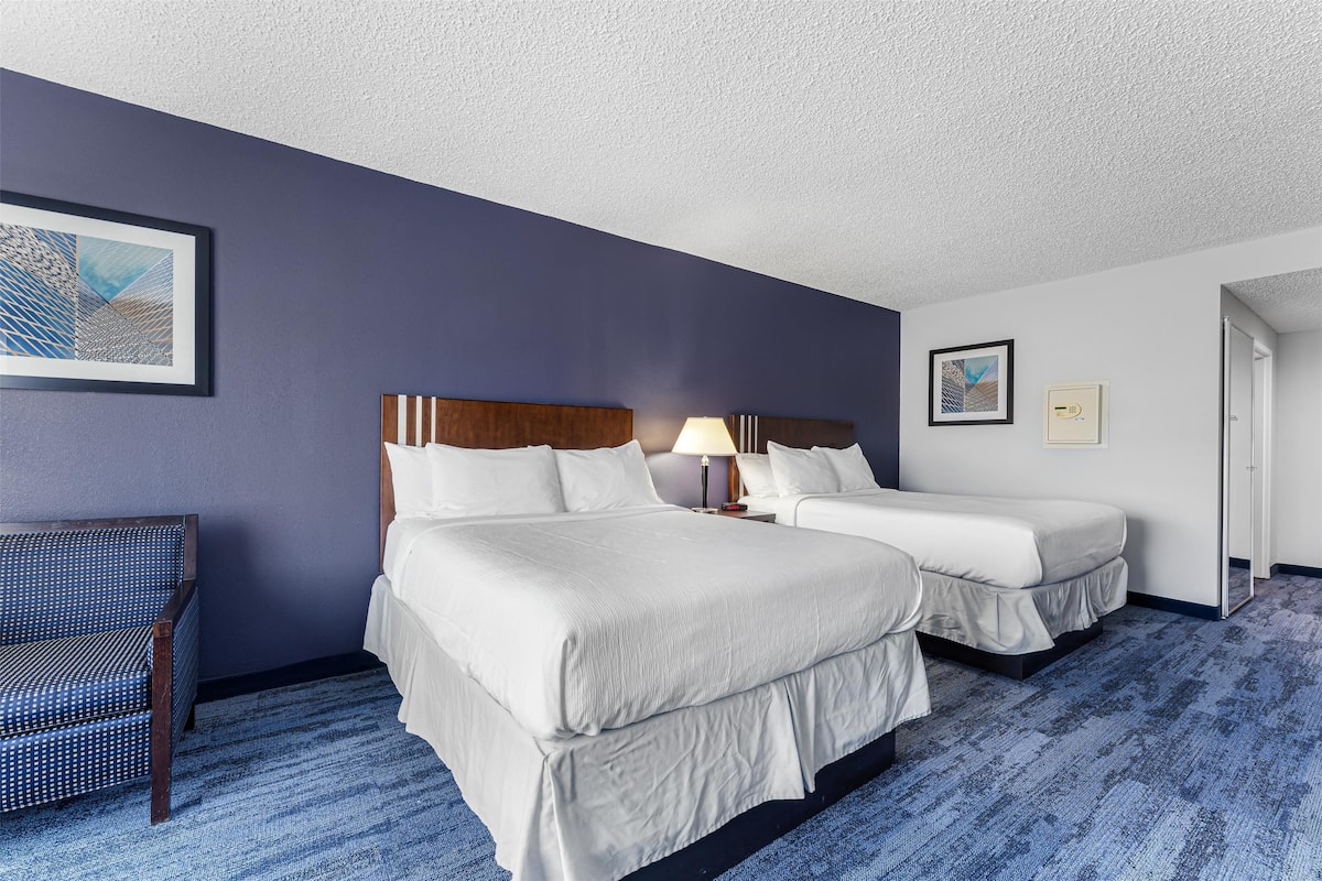 A hotel room with two beds, a chair, and artwork on the walls.