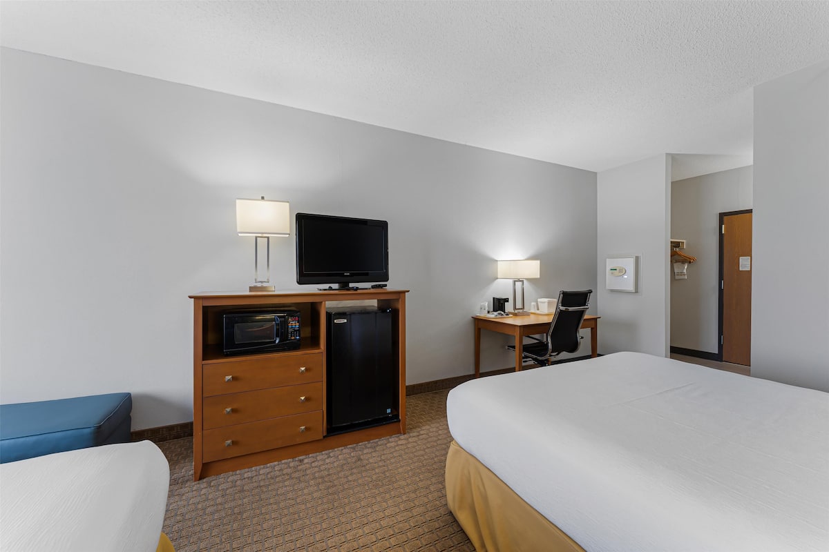 A hotel room with a bed, a desk with a computer, a microwave, and a television.