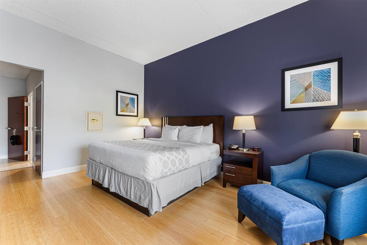 A hotel room with a large bed, a blue armchair, and a nightstand with a lamp.