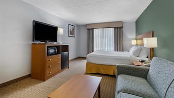 A hotel room with a bed, a sofa, a desk, a television, and a minibar.