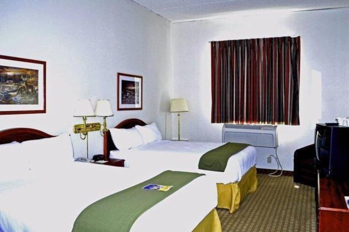 A hotel room with two beds, a desk, a television, and a window with curtains.