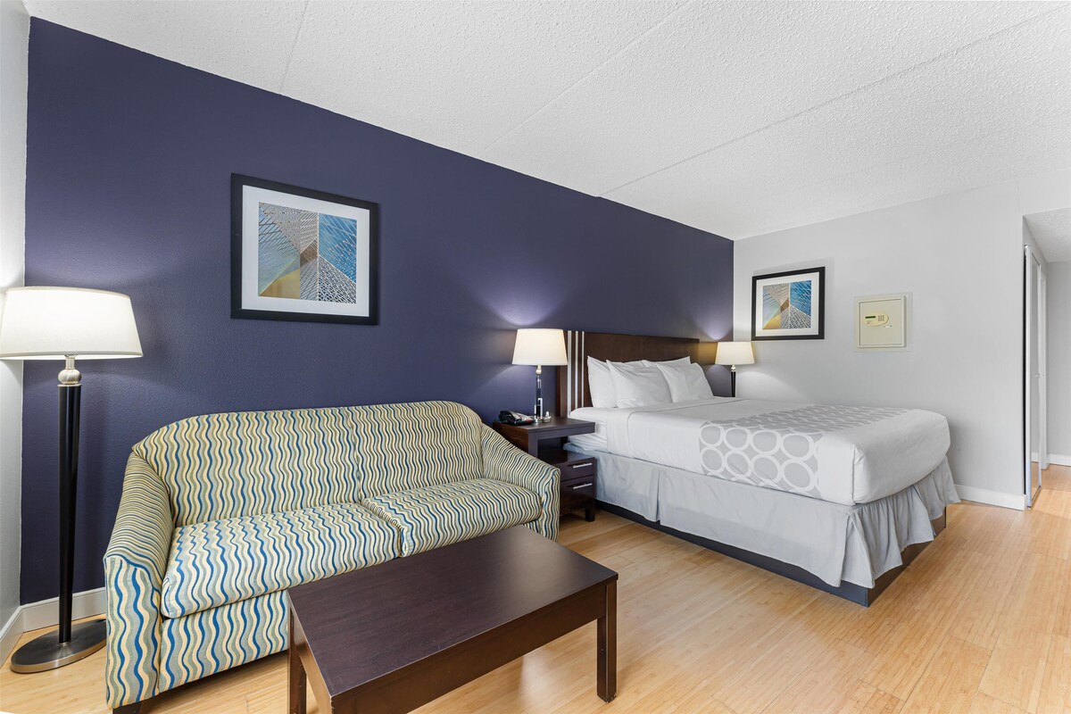 A hotel room with a sofa, a bed, a nightstand, and two lamps.