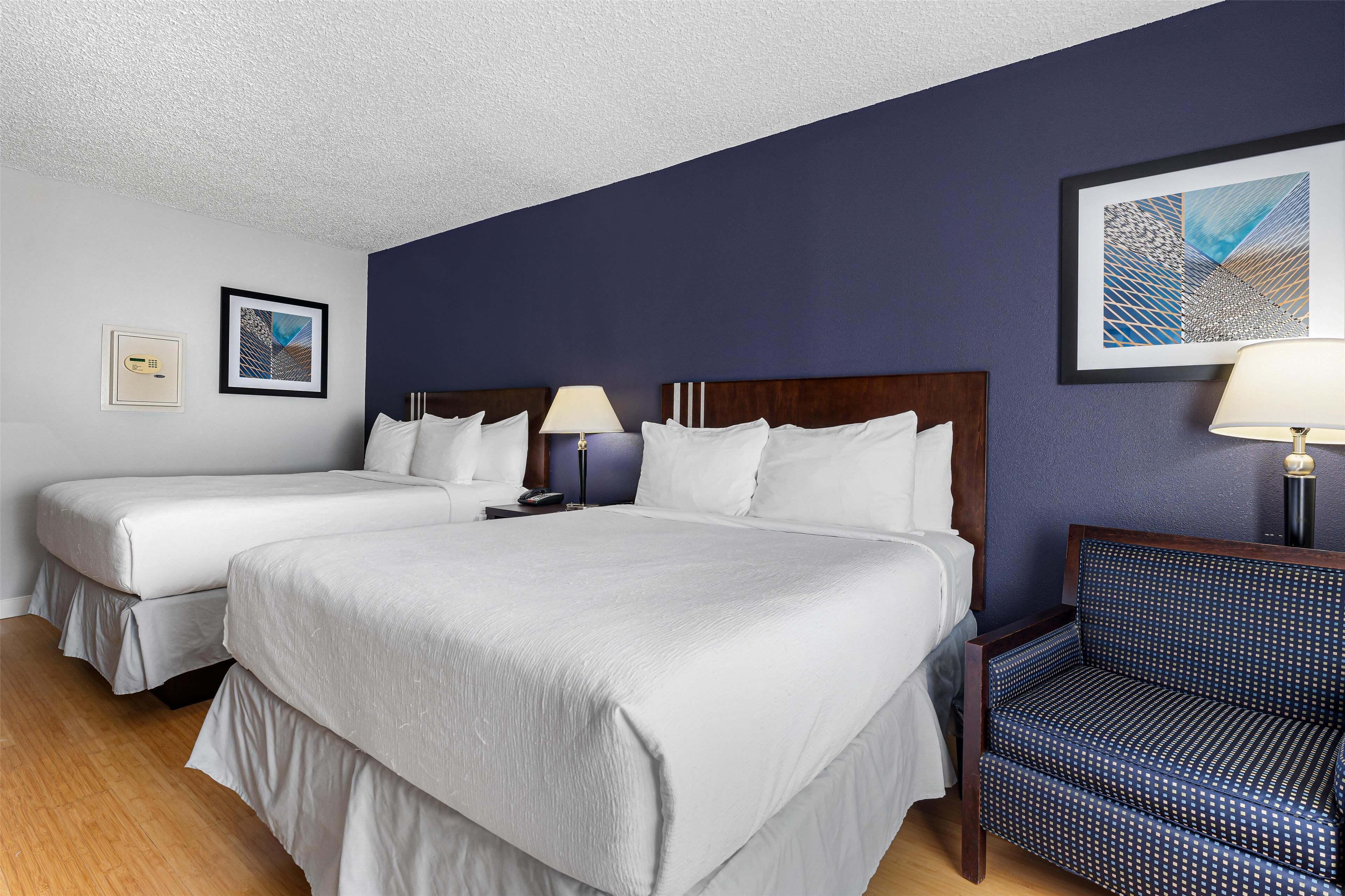 A hotel room with two beds, a chair, and artwork on the walls.