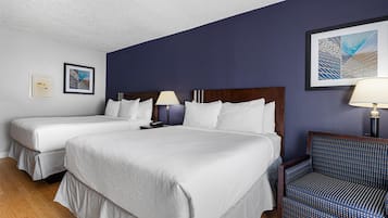 A hotel room with two beds, a chair, and artwork on the walls.