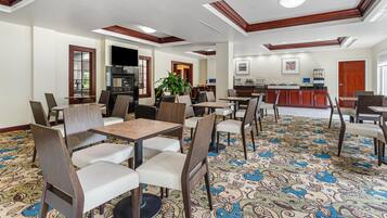 Un comedor de hotel con varias mesas y sillas, una cocina al fondo y una alfombra estampada.