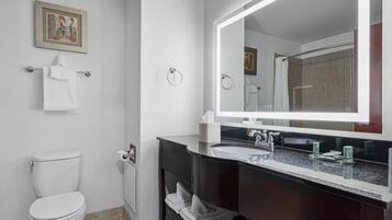 A modern bathroom with a white toilet, a dark vanity with a large mirror, and a framed picture on the wall.