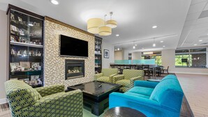 A spacious living area with patterned sofas, a fireplace, and a television. - Best Western Garden Inn (Bentleyville)