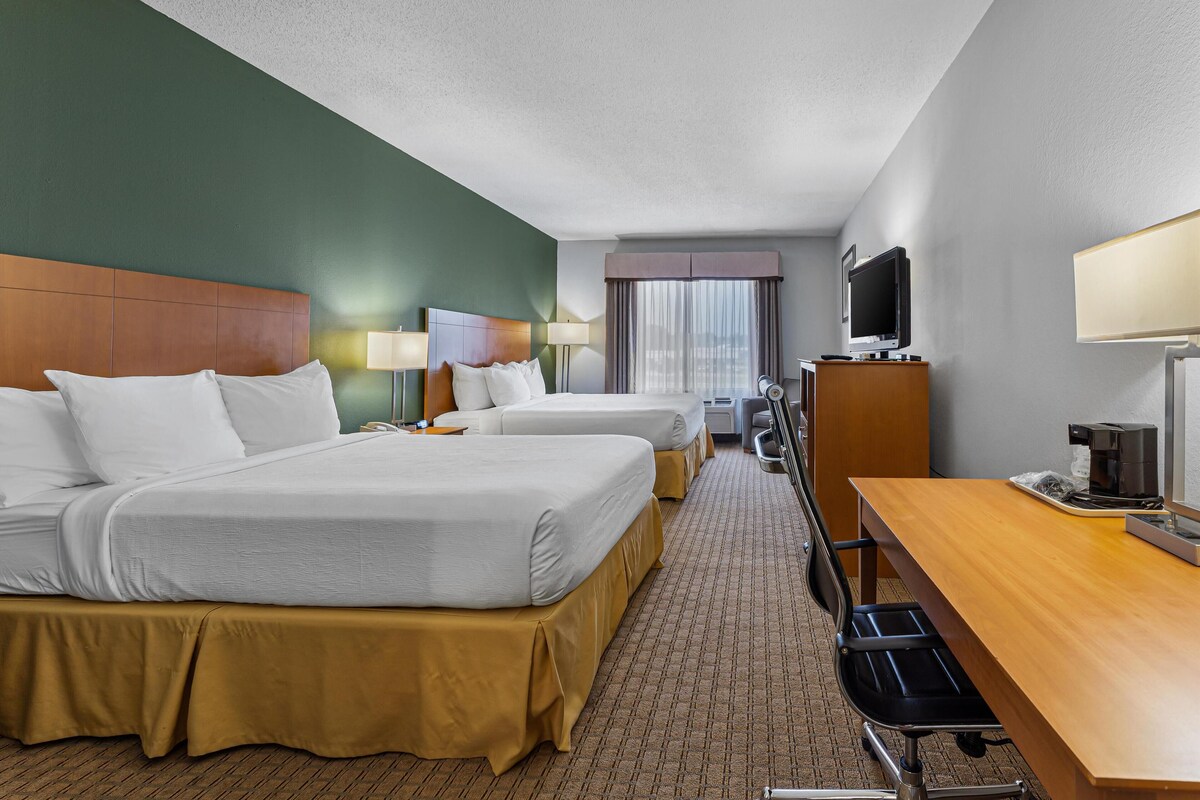 A hotel room with two beds, a desk, a television, and a window with curtains.
