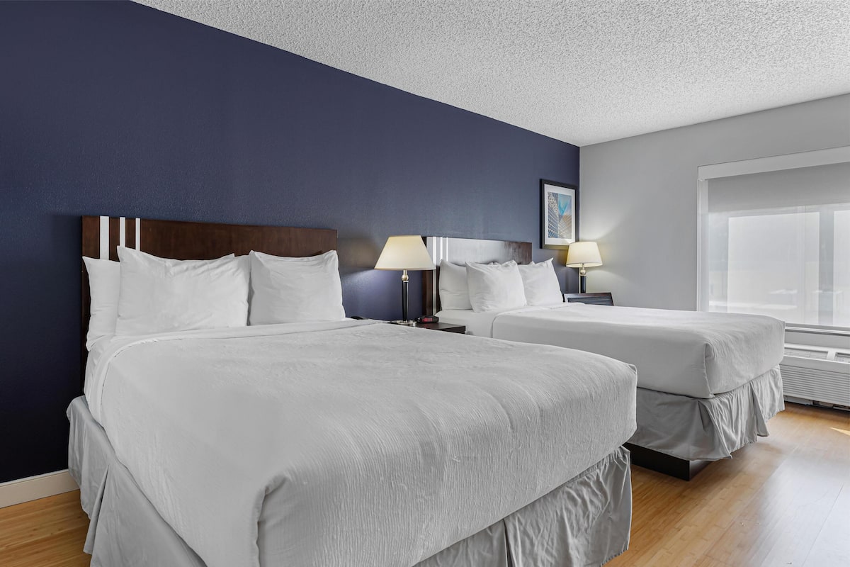 A hotel room with two beds, a large window, and a dark blue accent wall.