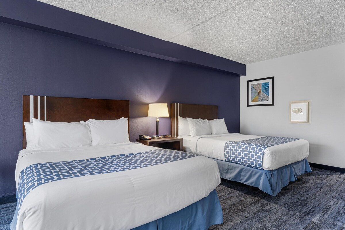 A hotel room with two beds, a nightstand with a lamp, and a framed picture on the wall.