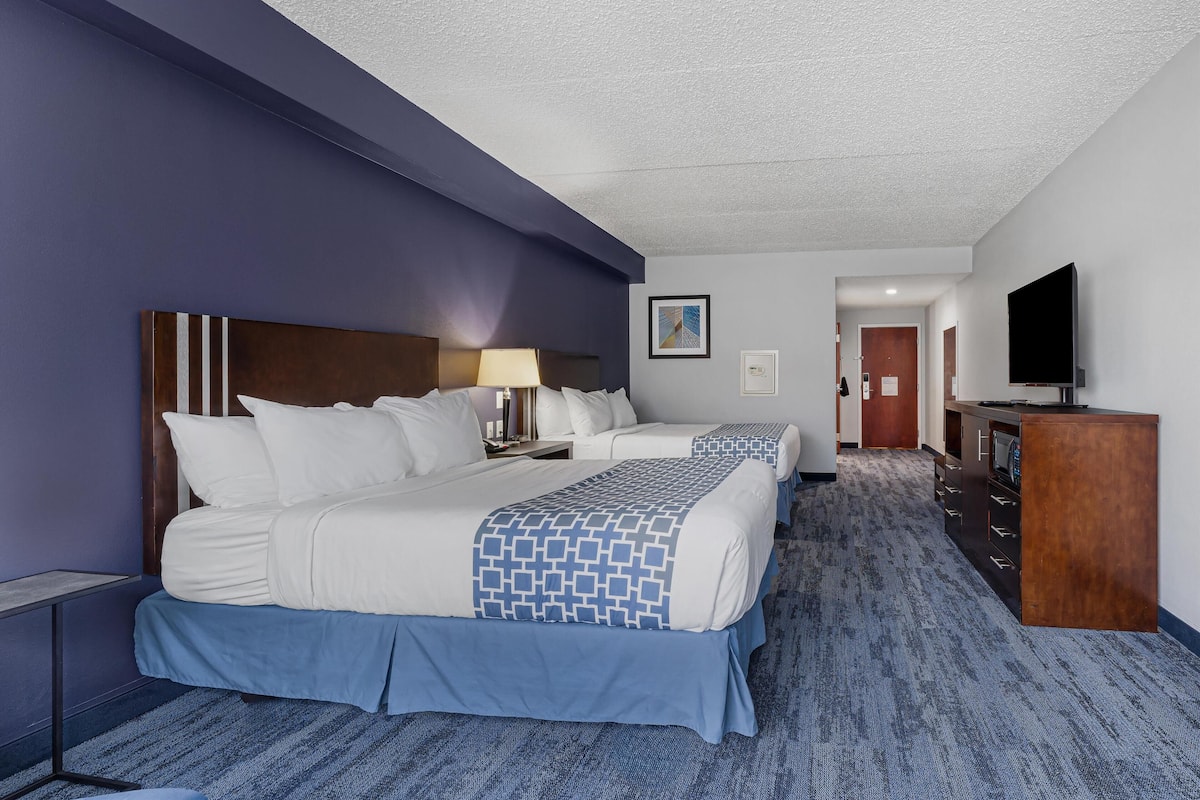 A hotel room with two beds, a desk, a dresser, and a television.