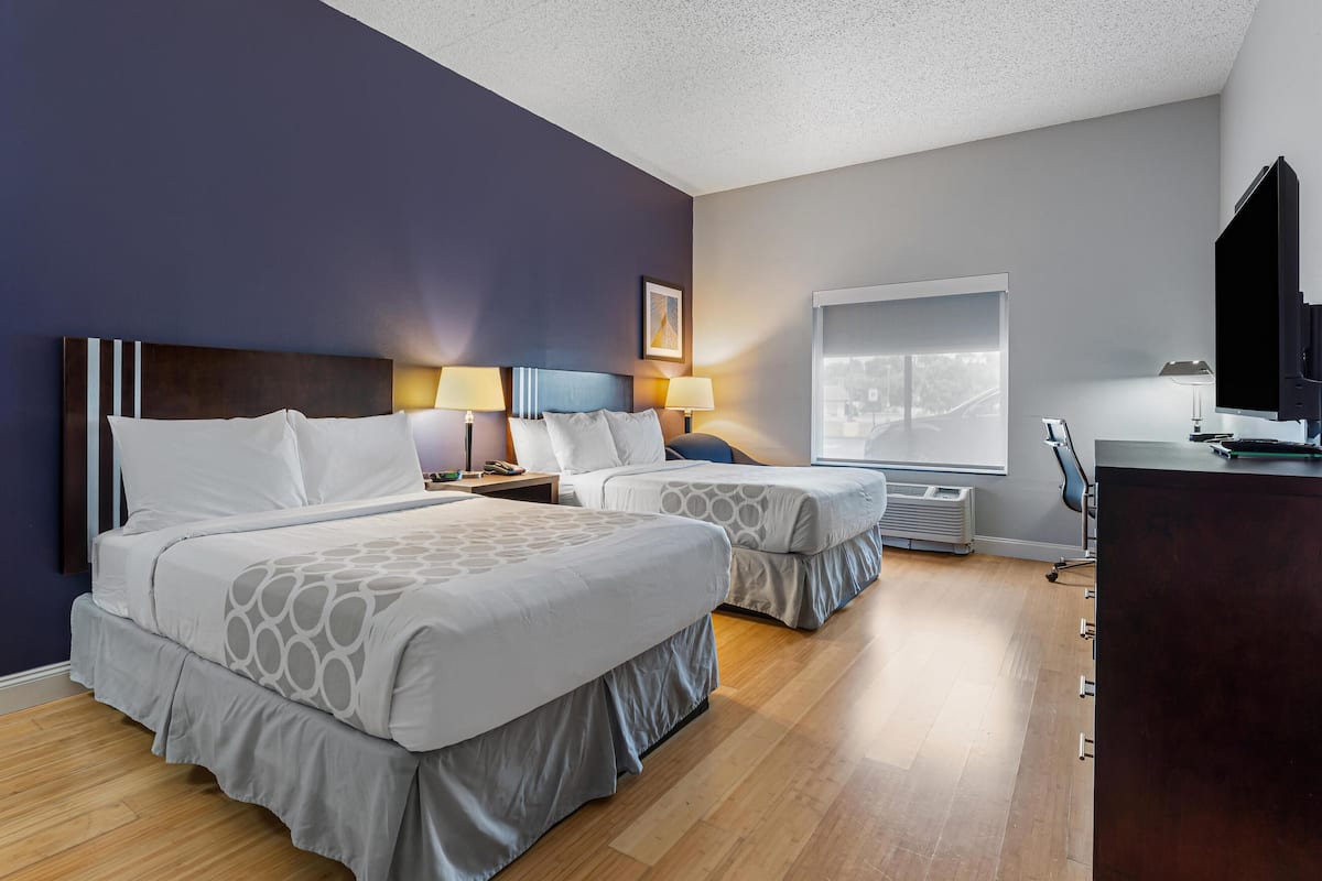 A hotel room with two beds, a desk, a TV, and a window with a city view.