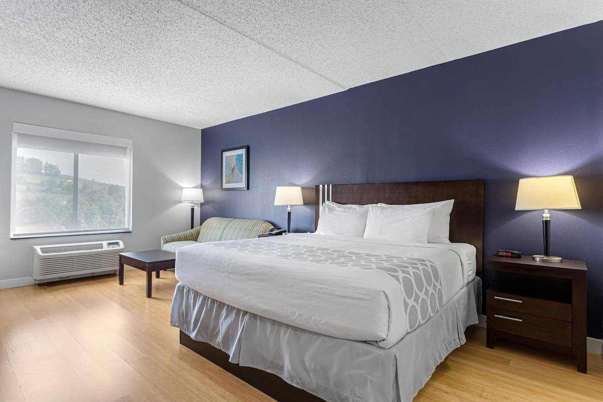 A hotel room with a large bed, two bedside tables with lamps, a window with a view, and a wall-mounted heater.