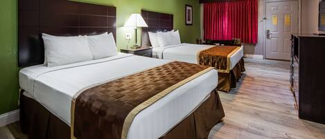 A hotel room with two beds, a desk, a ceiling fan, and a red curtain.
