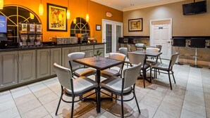 A hotel room with a dining area featuring a table and chairs, a kitchen area with appliances, and a TV mounted on the wall. - Bestway Inn (Kaufman)