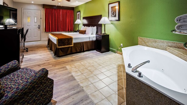 A hotel room with a bed, a large bathtub, a desk with a lamp, a chair, and a television. - Bestway Inn (Kaufman)