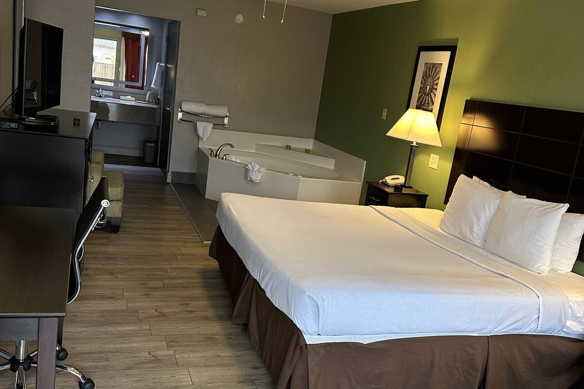 A hotel room with a bed, desk, chair, and a bathroom with a bathtub.