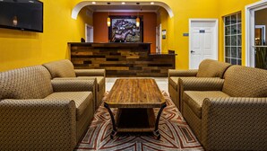 A reception area with a wooden reception desk, two patterned sofas, a patterned rug, and a stained glass window. - Bestway Inn (Kaufman)