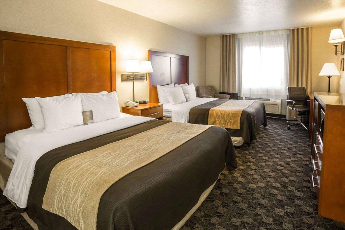 A hotel room with two beds, a desk, a chair, a lamp, and a window with curtains.