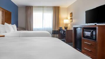 A hotel room with two beds, a desk with a chair, a flat-screen TV, a microwave, and a window with curtains.