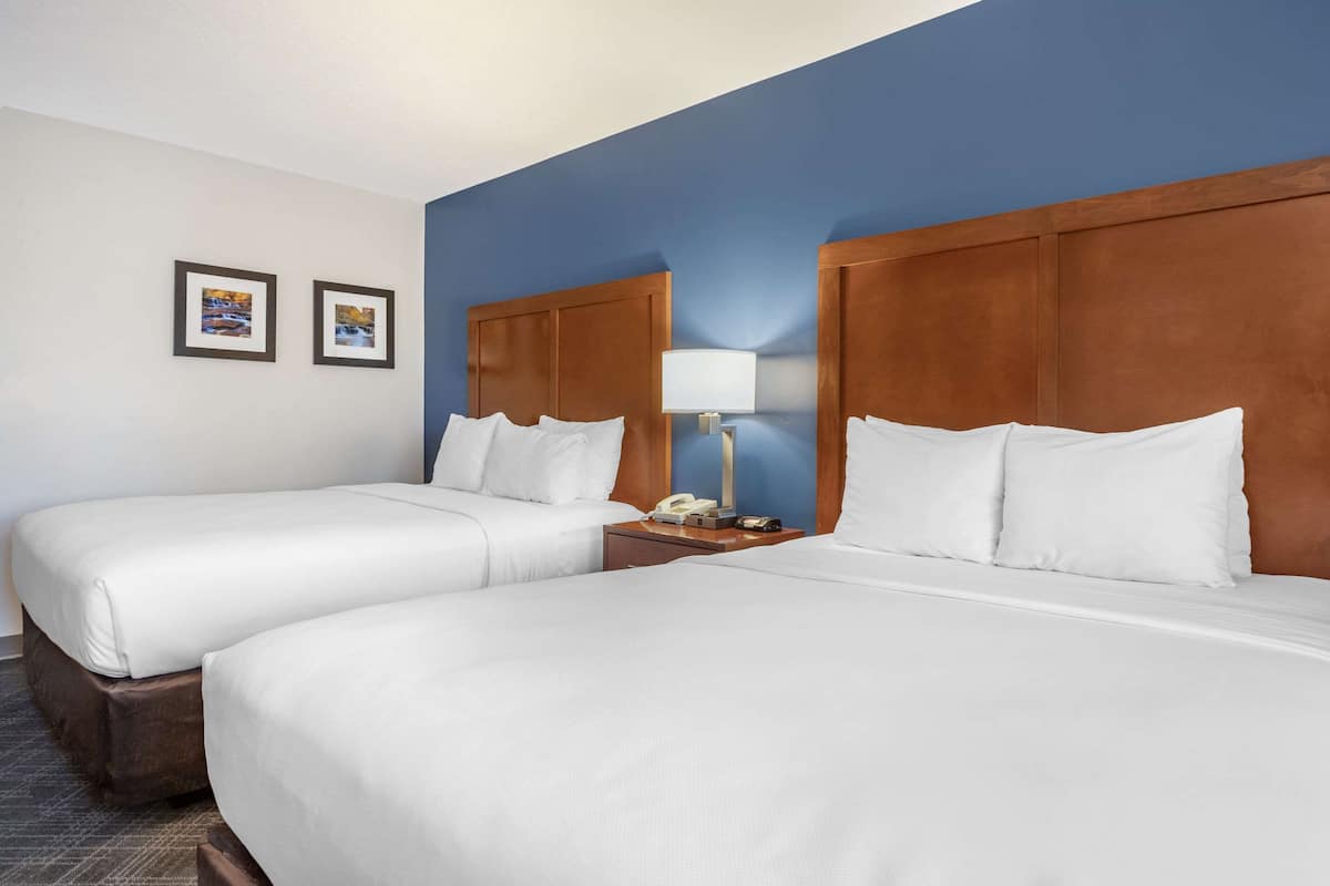 A hotel room with two beds, a wooden headboard, a nightstand with a lamp, and two framed pictures on the wall.