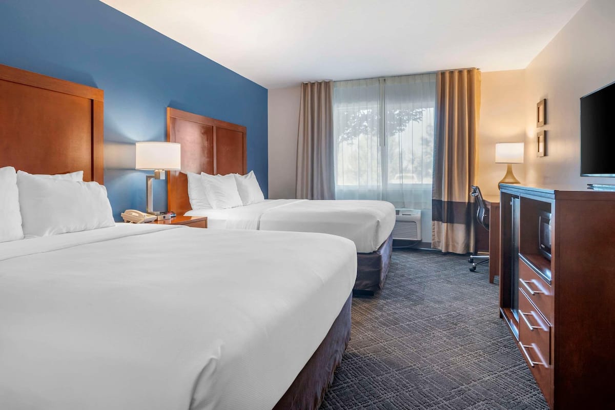 A hotel room with two beds, a desk, a television, and a window with curtains.