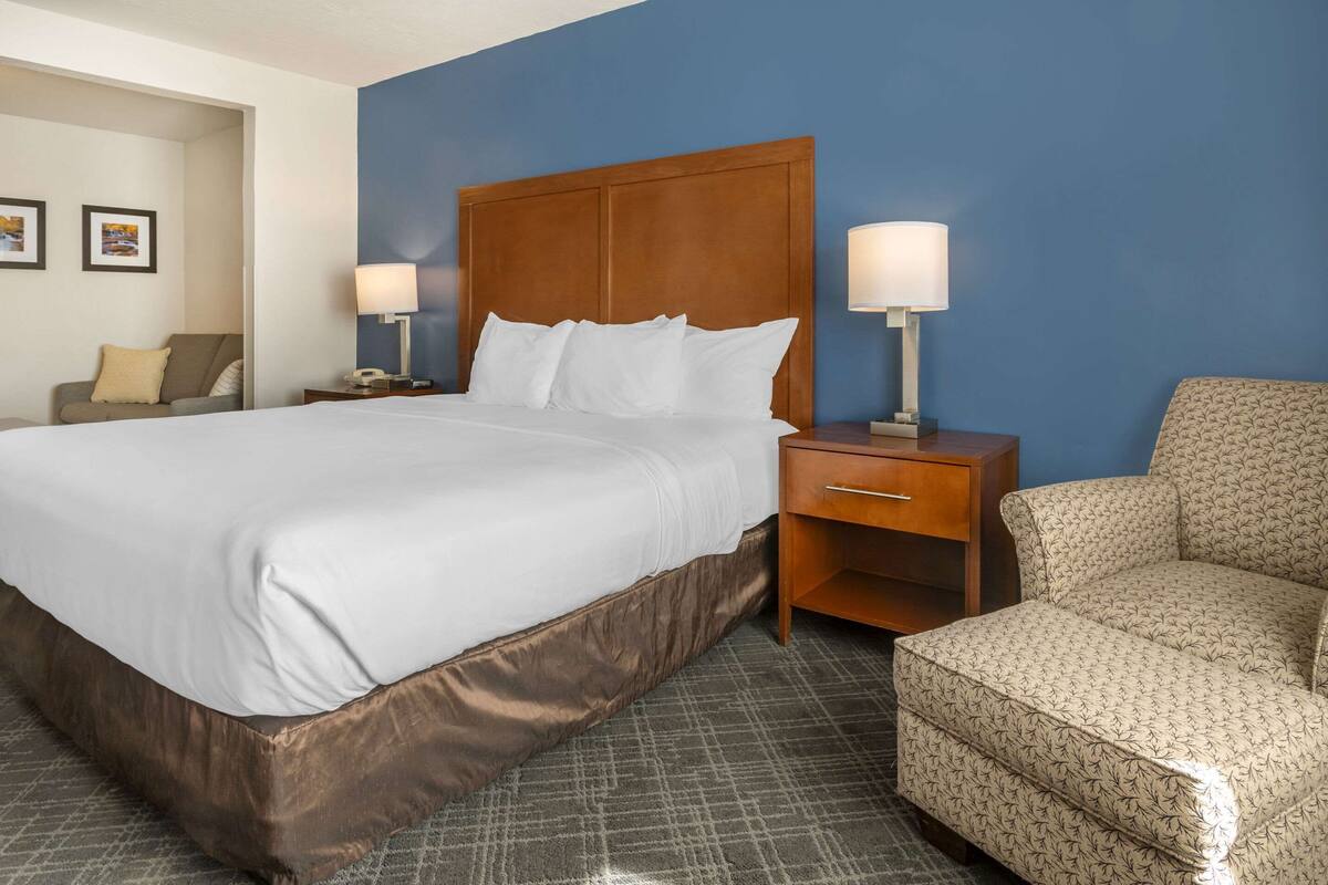 A hotel room with a large bed, two bedside tables with lamps, a chair, and a blue accent wall.