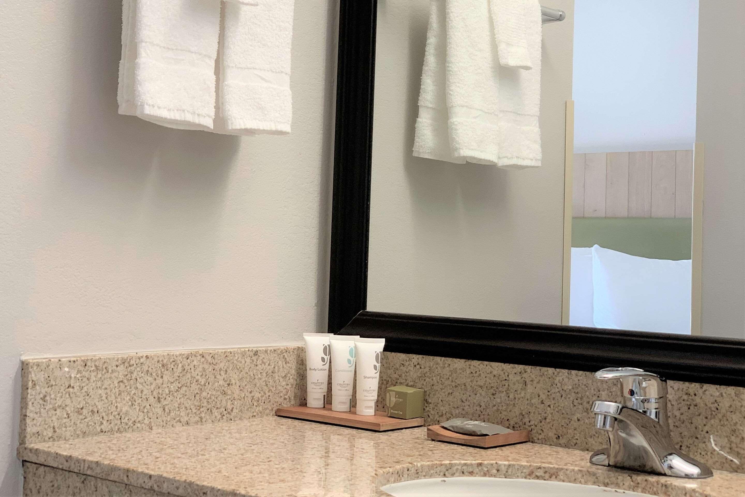Un baño con encimera de granito, lavamanos, espejo y artículos de aseo.