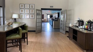 A modern kitchen with a dining area, featuring a wooden floor, a dining table with chairs, a kitchen counter with appliances, and framed artwork on the walls.