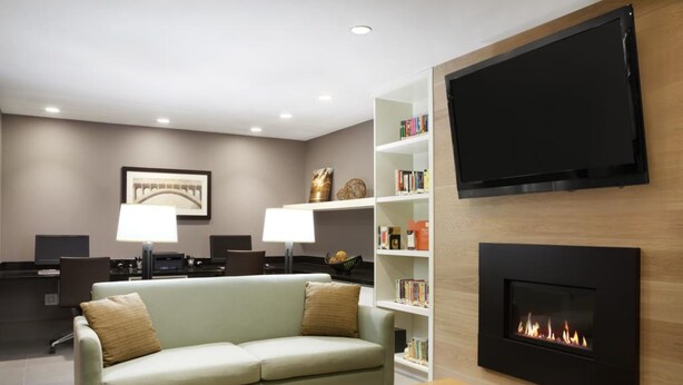 A modern living room with a sofa, a coffee table, a fireplace, a TV mounted on the wall, and a bookshelf with books.