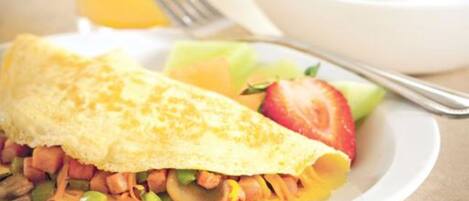 Un plato de desayuno con una tortilla, verduras, fruta, un vaso de zumo de naranja y un bol de yogur con frutos rojos.