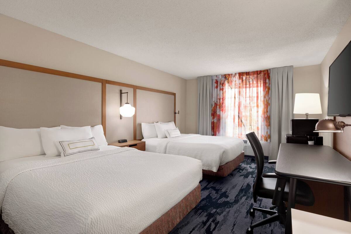 Ein Hotelzimmer mit zwei Betten, einem Schreibtisch, einem Stuhl, einem Fernseher und einer Lampe.