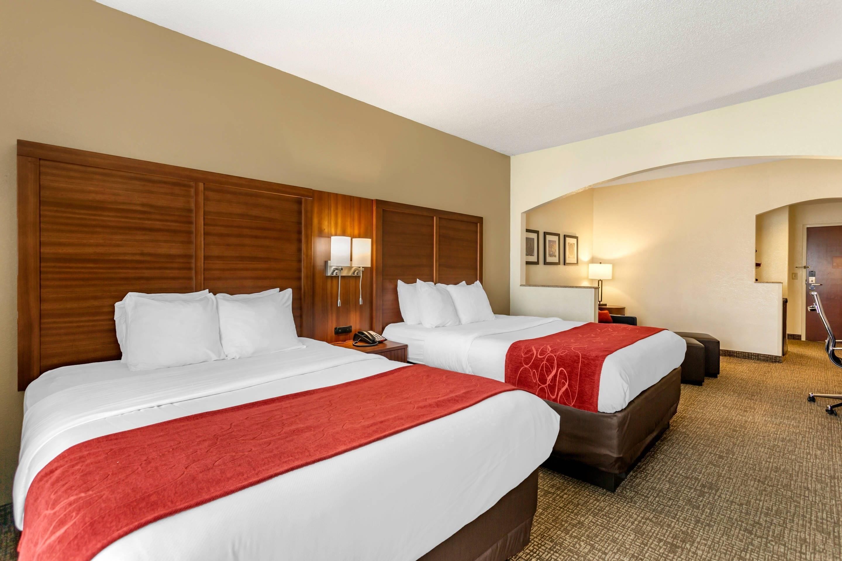 A hotel room with two beds, a wooden headboard, a desk, and a chair.