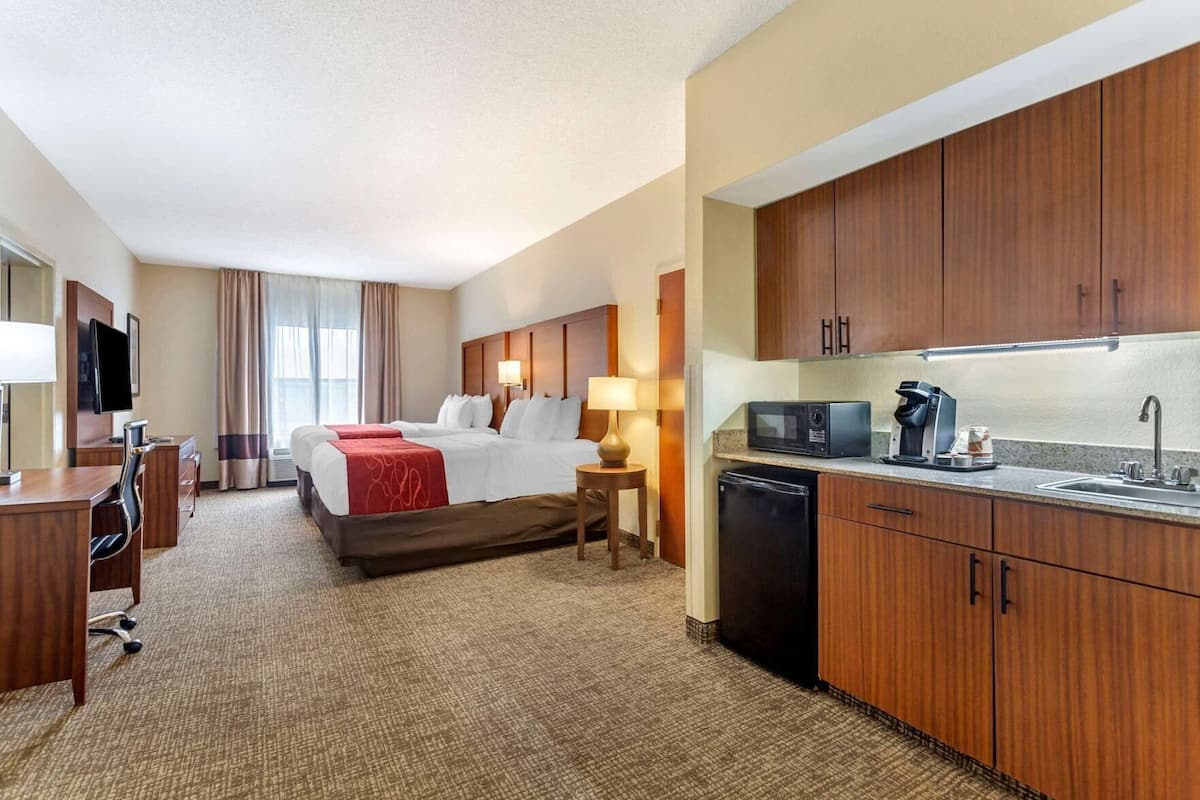A hotel room with a bed, desk, chair, and kitchenette.