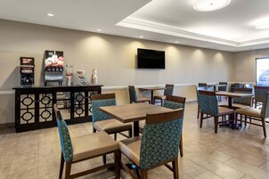 Um restaurante com área de bar, mesas e cadeiras, e uma televisão de tela plana na parede.