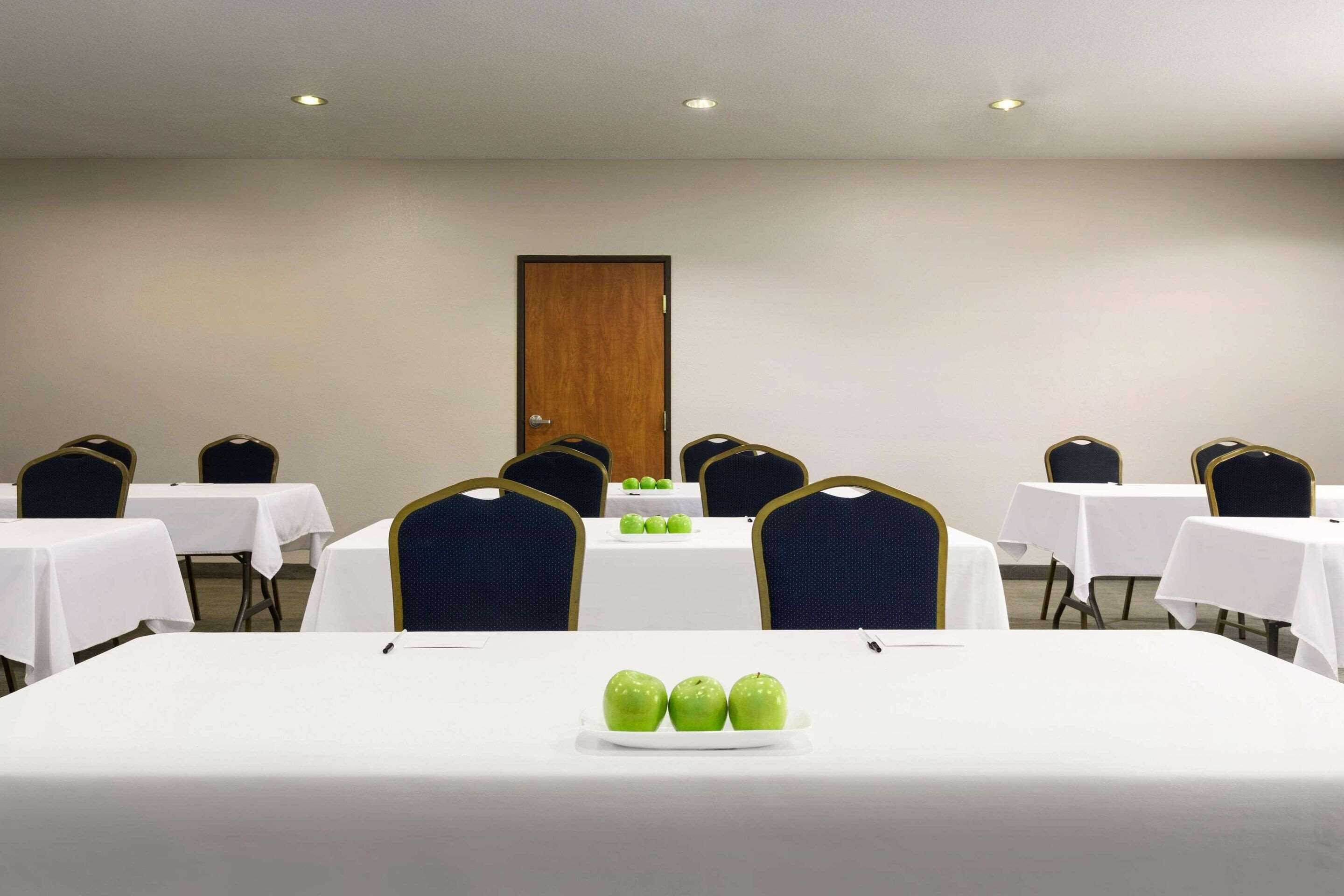 A conference room with white tables and chairs, a wooden door, and a plate of green apples on the table.