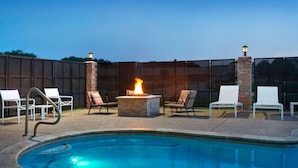 A swimming pool with a fire pit and lounge chairs.