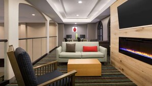 A hotel lobby with a sofa, a wooden chair, a coffee table, a flat-screen TV, and a fireplace.