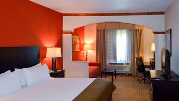 A hotel room with a large bed, a desk with a chair, a television, and a window with curtains.