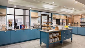A modern kitchen with blue cabinets, a central island with food displays, and a coffee station.